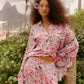 Woman in a pink floral shirt and skirt set standing outdoors with mountains and palm trees in the background