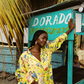 Woman in a colorful yellow outfit standing next to a Dorado Restaurant sign.
