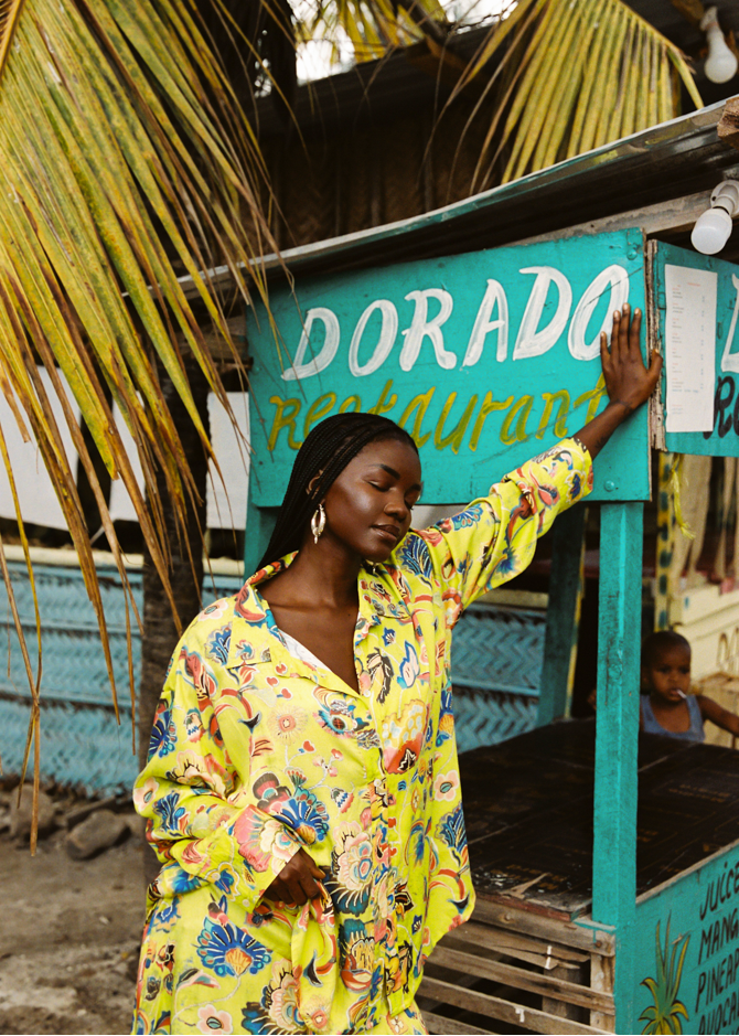 Woman in a colorful yellow outfit standing next to a Dorado Restaurant sign.