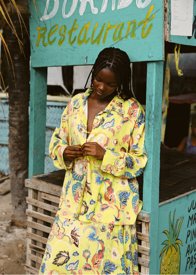 Woman in a colorful yellow set standing in front of a restaurant sign.