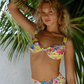 Woman wearing a colorful yellow floral bikini against a tropical background with palm leaves.