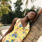 Woman in a yellow floral dress leaning against a tree with palm trees in the background