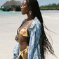 Woman in a colorful yellow bikini with a blue floral cover-up on a beach.