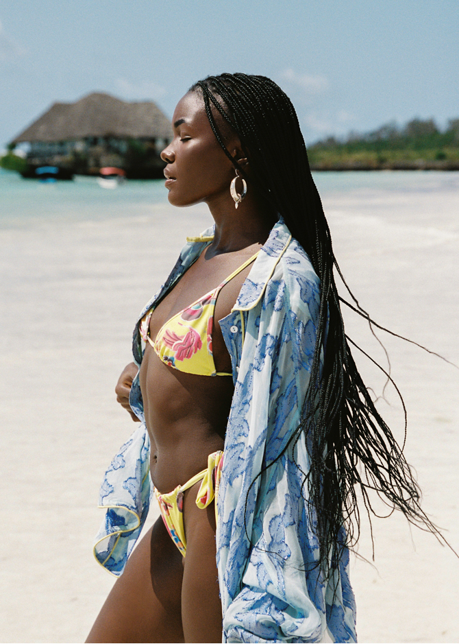 Woman in a colorful yellow bikini with a blue floral cover-up on a beach.