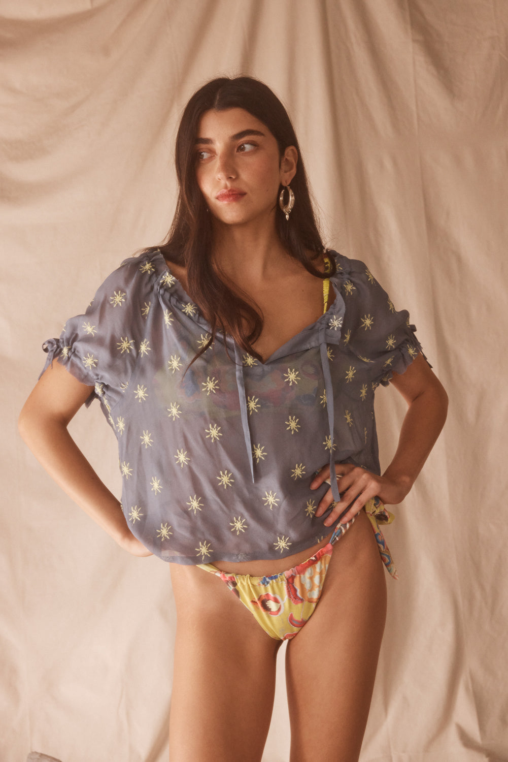 Woman wearing a colorful yellow bikini with a matching top against a beige background
