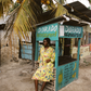 Woman in a yellow floral set sitting in front of a Dorado Restaurant stand with palm trees in the background.