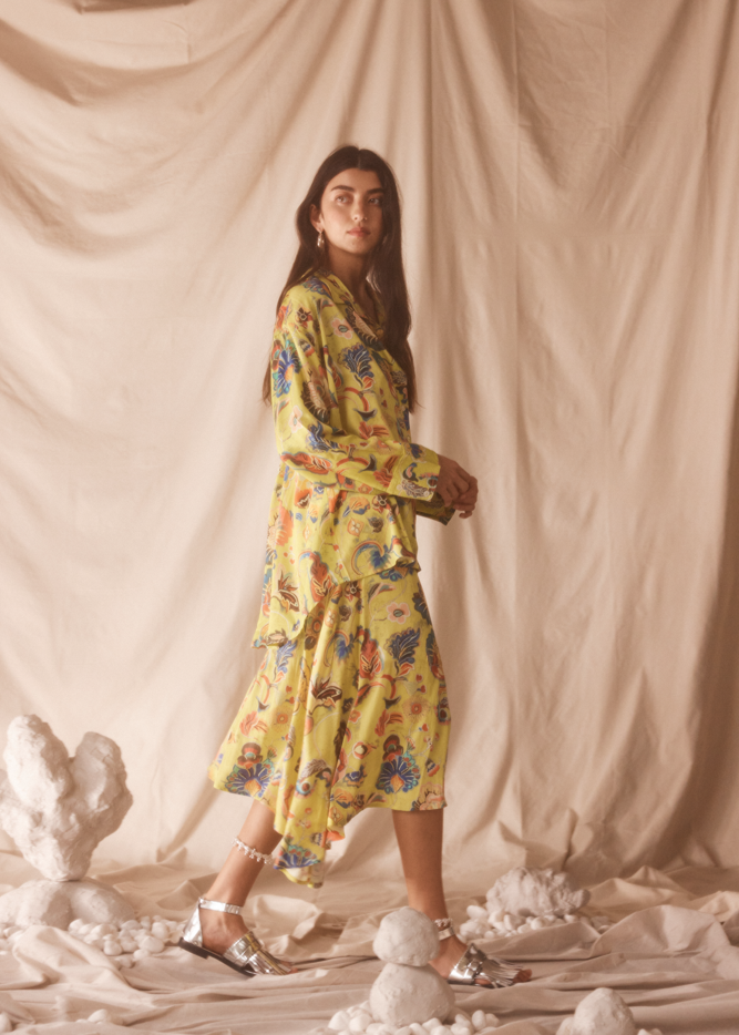 Woman in a yellow floral set standing against a beige curtain backdrop