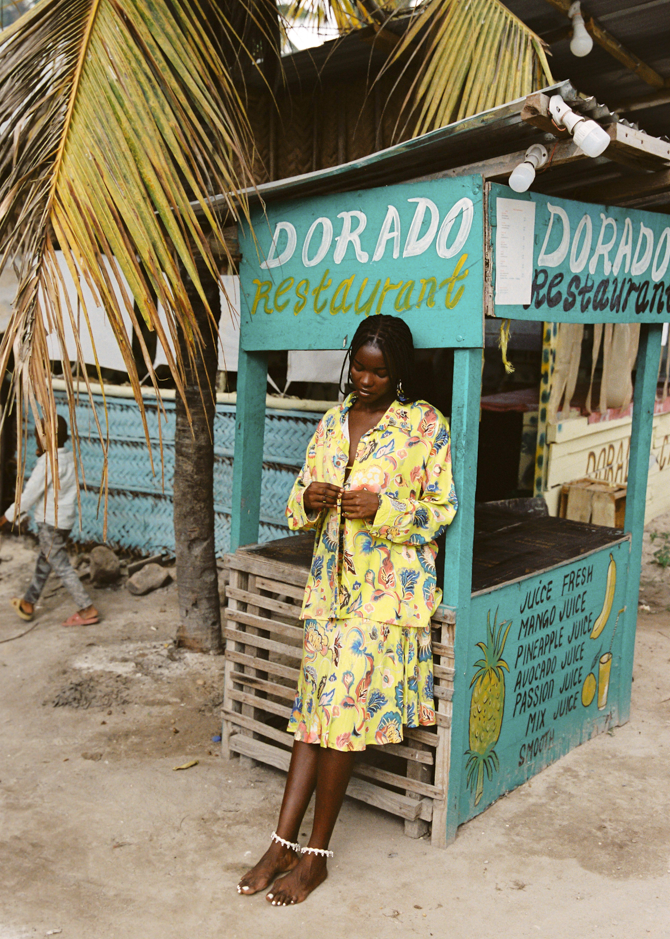 Woman in a yellow floral set standing in front of a Dorado Restaurant stand.