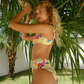 Woman in a colorful yellow bikini standing under palm trees