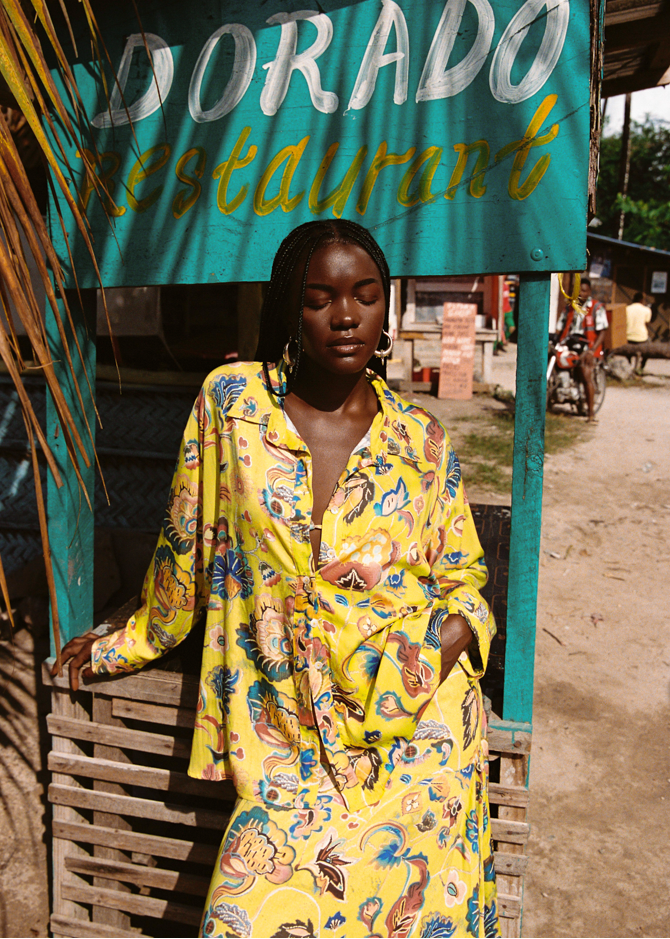 Woman in a colorful set standing in front of a Dorado Restaurant sign.