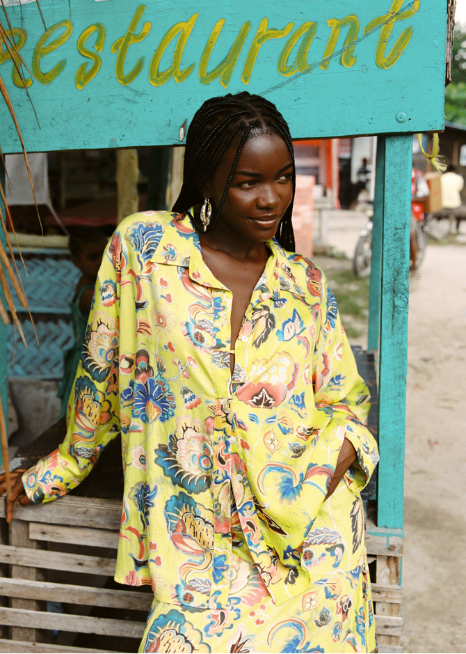 Woman wearing a colorful floral set standing in front of a restaurant sign.