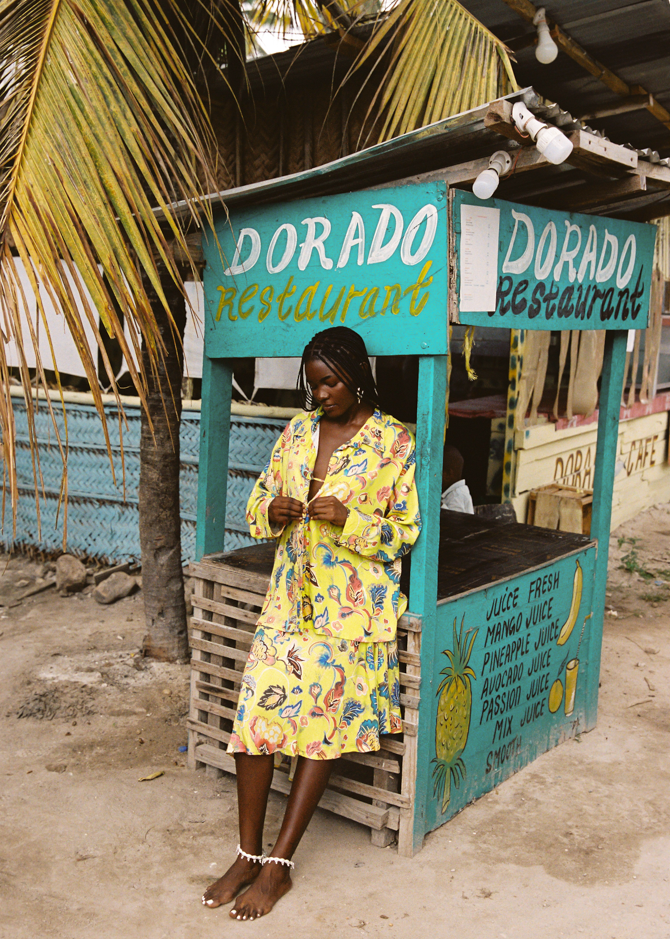 Woman in a yellow set standing in front of a Dorado Restaurant sign.