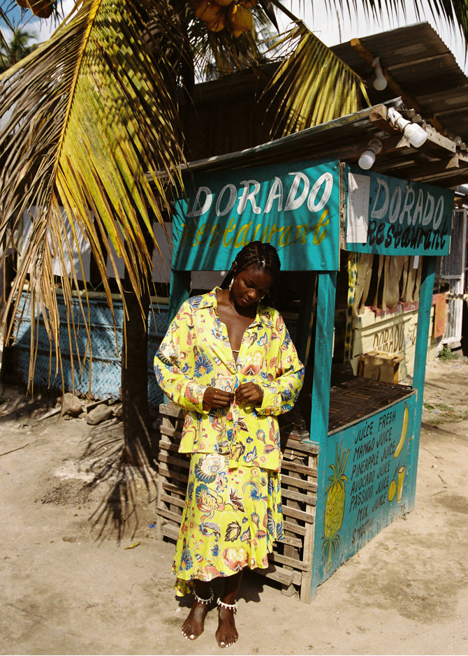 Woman in a yellow floral set standing in front of a Dorado restaurant stand.