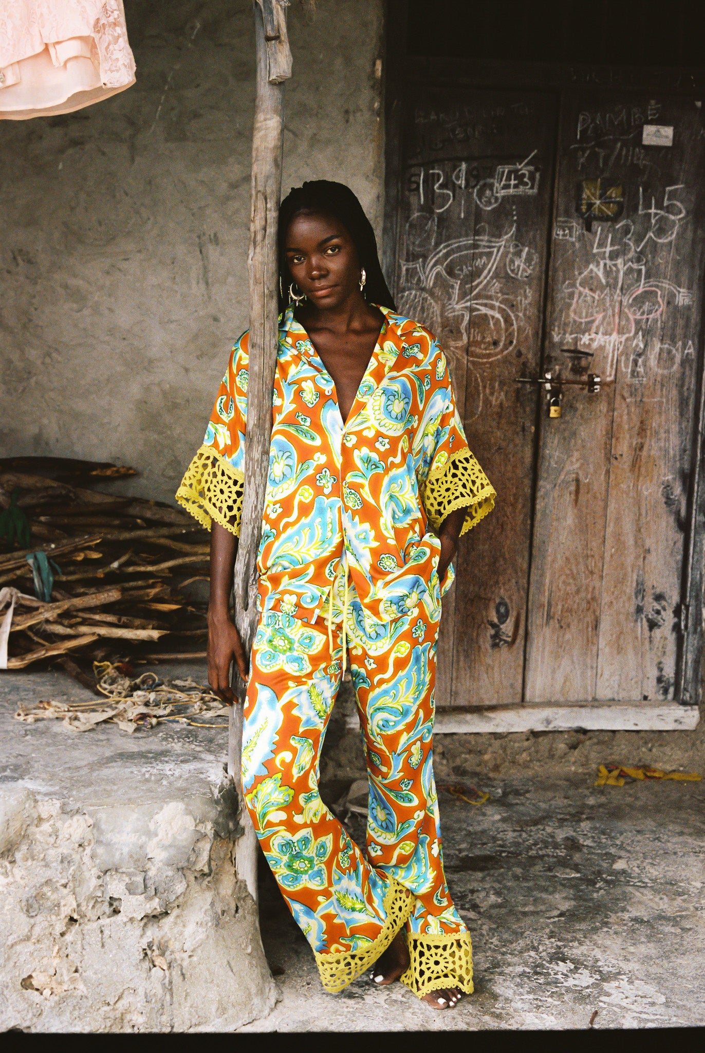 Woman wearing colourful orange, blue and green print flared pant and shirt set with green lace trim detailing