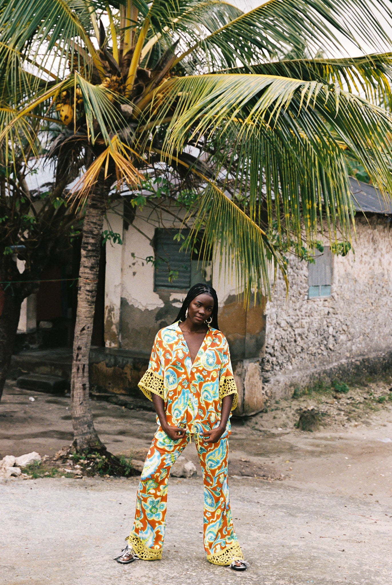 Woman wearing orange, blue and green patterned shirt and flared pant set with lime green embroided trim.