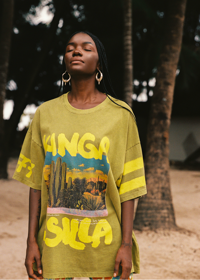 Woman wearing a lime green oversized t-shirt with colorful desert graphics and text, standing outdoors.