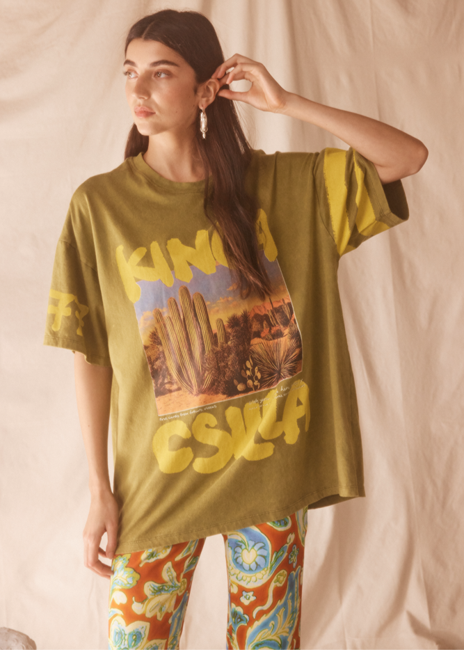 Person wearing a lime green desert graphic t-shirt with colorful pants against a plain background
