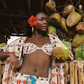 Woman in a tropical setting holding coconuts with hanging coconuts in the background wearing pink floral set