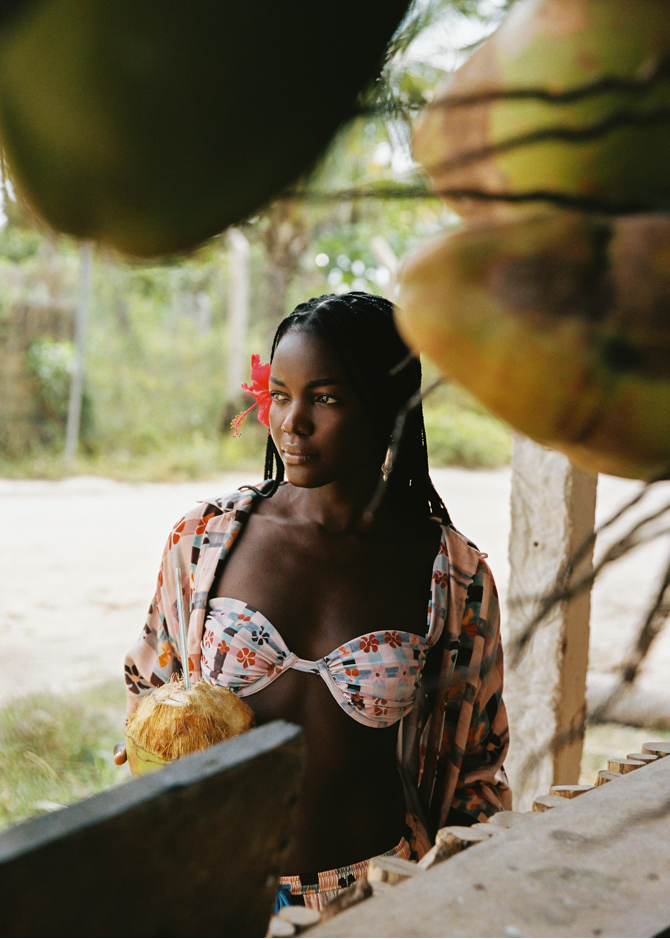 Woman in a tropical setting holding coconuts wearing matching pink patterned set and bikini top