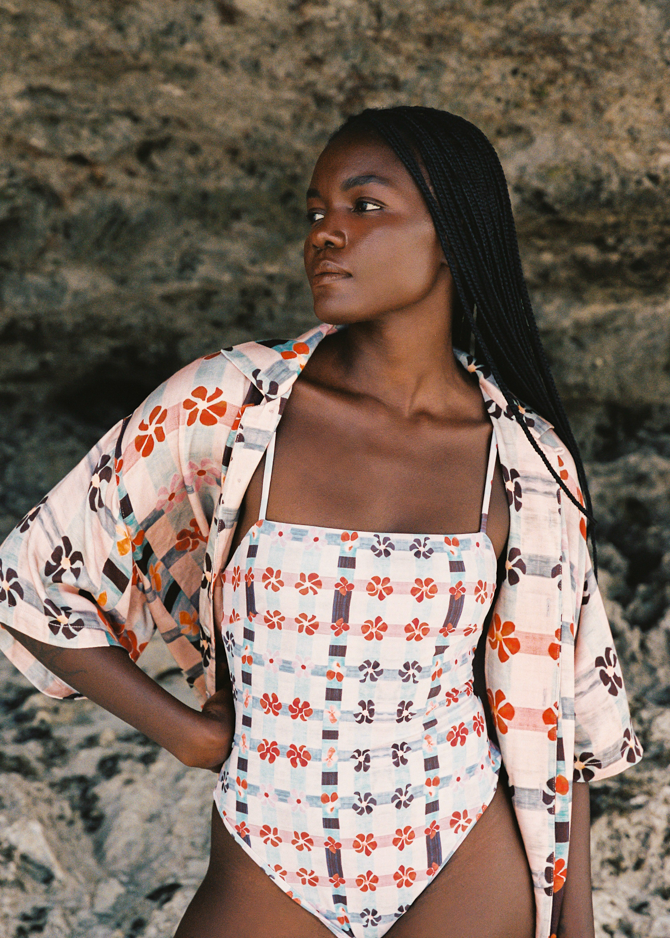 Woman wearing a pink floral swimsuit and cover-up against a stone wall.