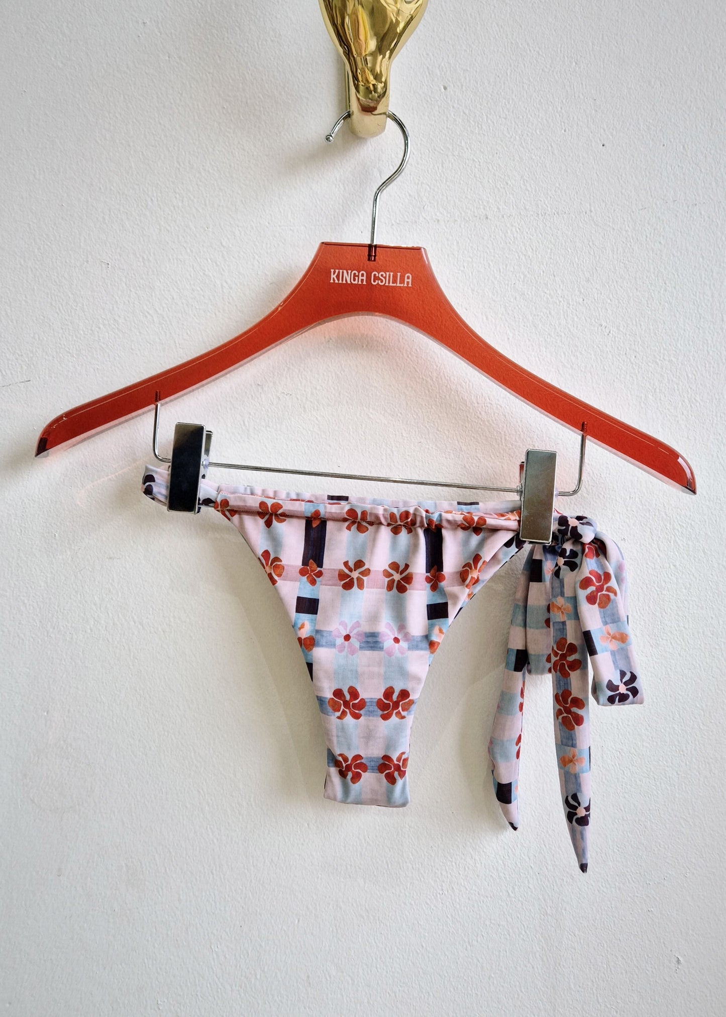 Multicolored patterned bikini bottom on a red hanger against a white background