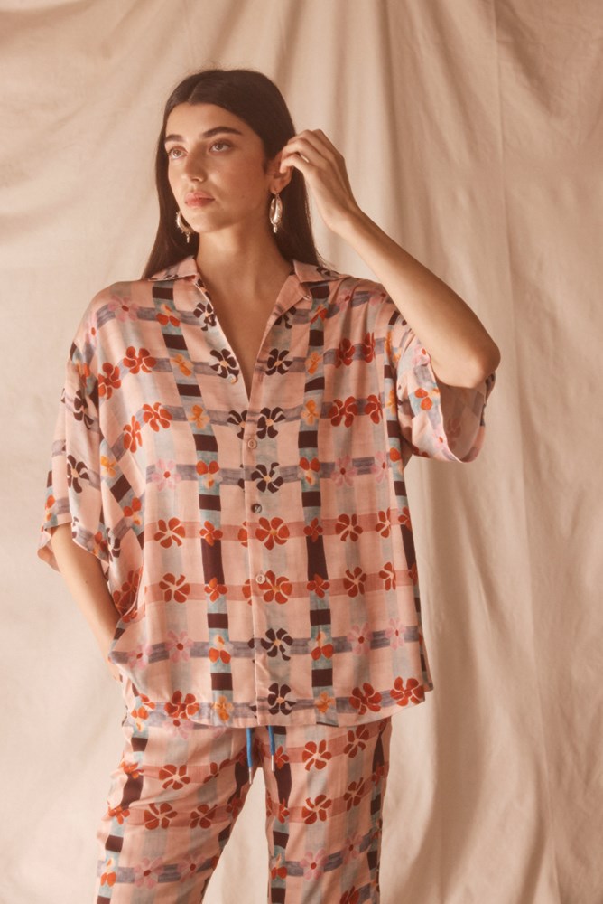 Woman wearing a pink patterned shirt and pants against a beige background