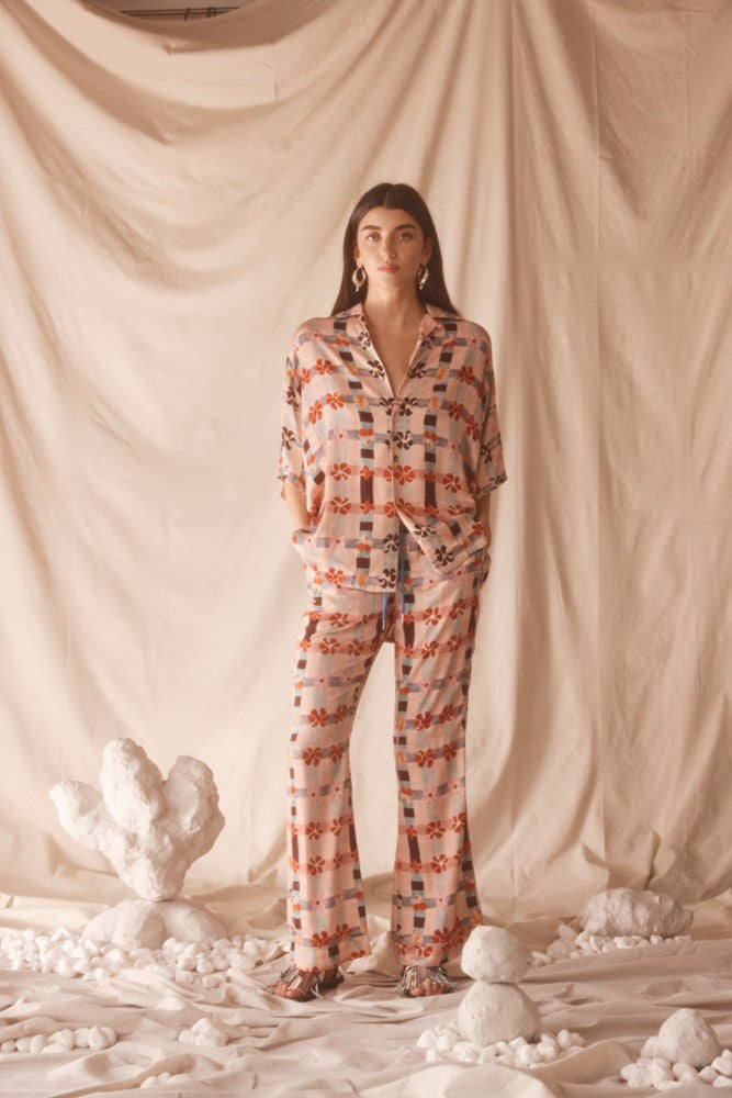 Woman wearing a pink patterned set standing against a beige curtain with desert-themed decor.