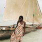 Woman in a pink floral dress standing in shallow water near a traditional sailboat.
