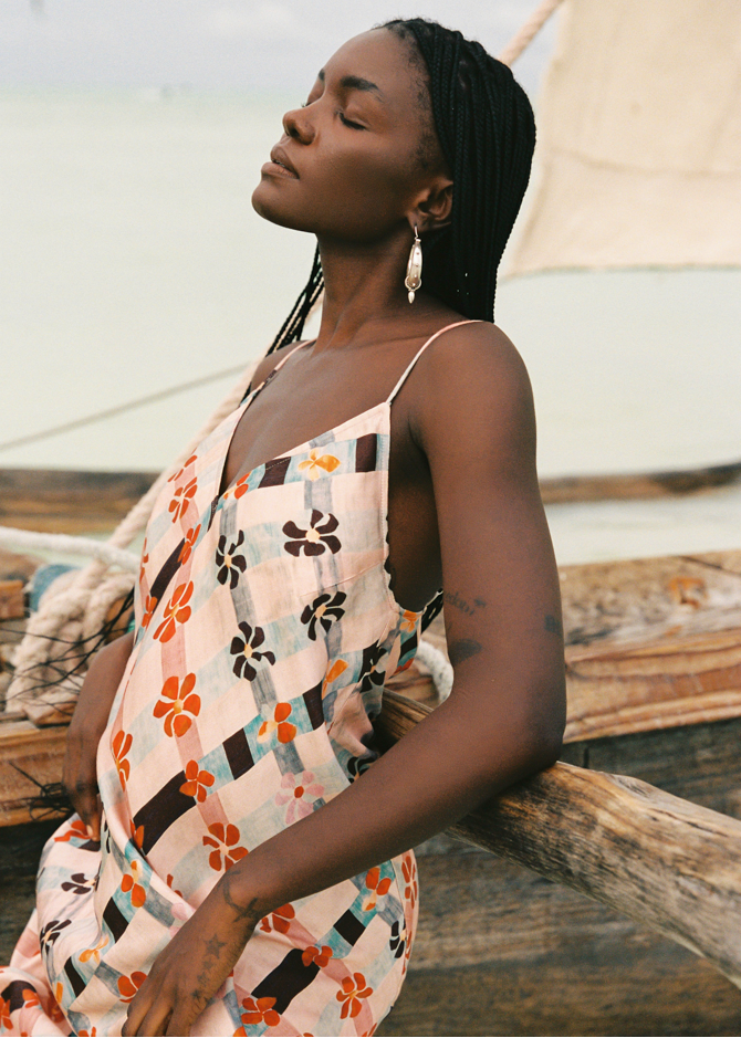 Woman in a pink floral dress sitting by a sailboat on a beach