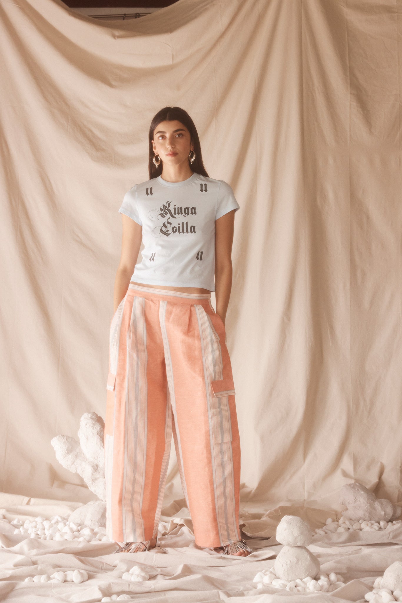 Woman wearing linen-cotton wide leg pants in peach, blue and ivory coastal stripes with side pockets and elastic waistband.