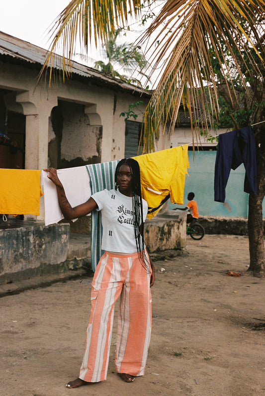 Woman wearing linen-cotton wide leg pants in peach, blue and ivory coastal stripes with side pockets and elastic waistband.