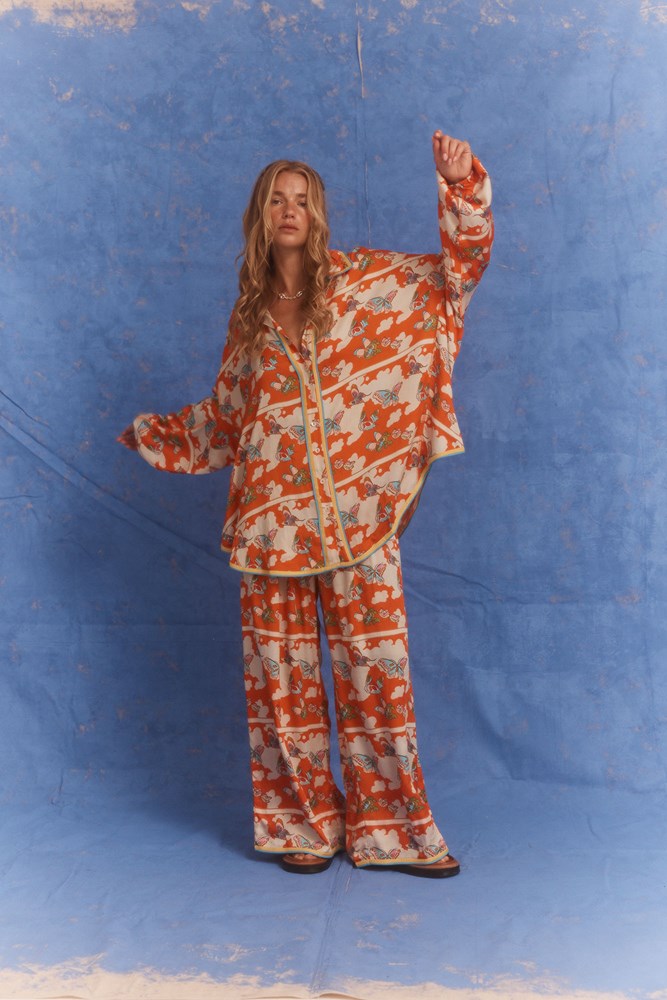 Woman in an orange patterned outfit with cloud/butterfly print standing in an architectural hallway, holding a map.
