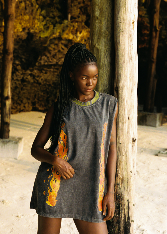 Woman wearing a sleeveless tank with colorful flame patterns leaning against a wooden wall.