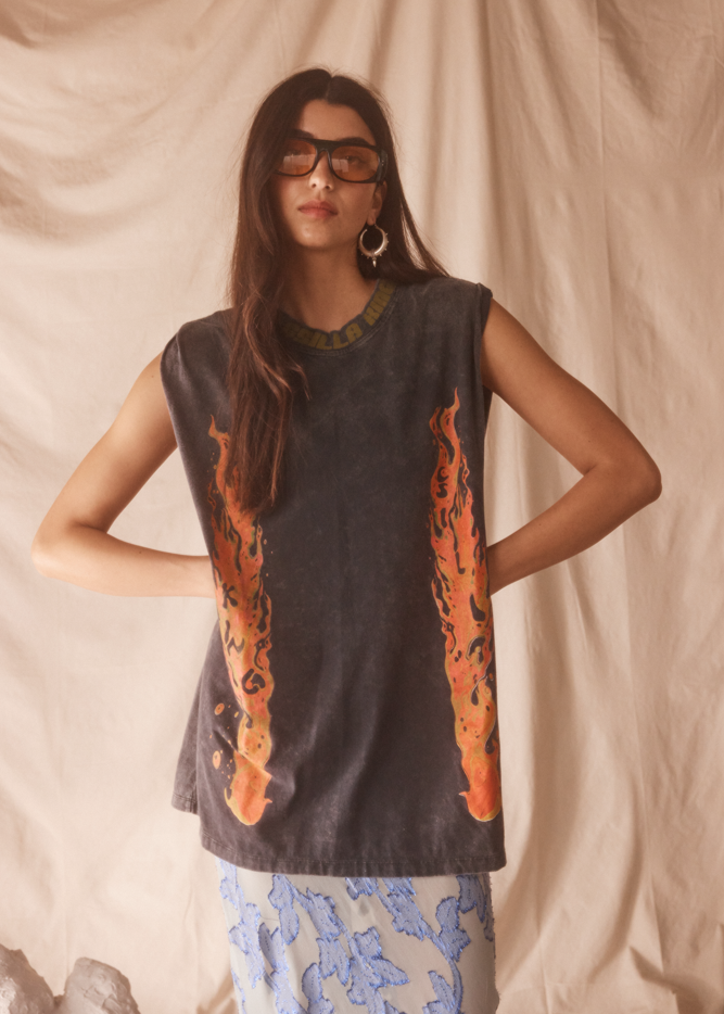 Woman wearing a sleeveless black top with orange flame patterns against a beige background