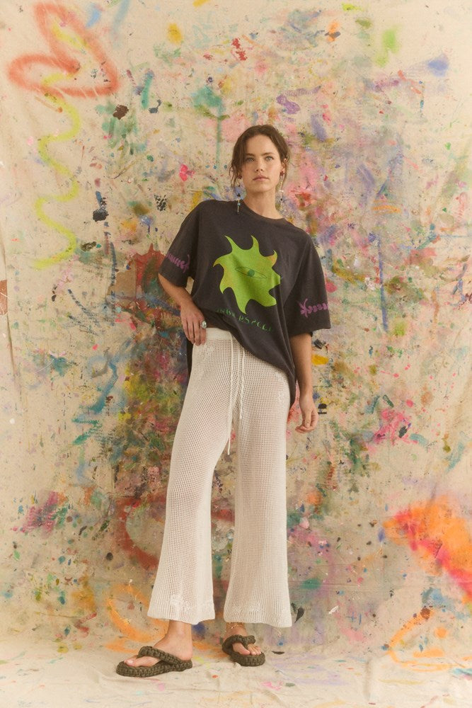 women in a graphic tee with a sun logo and white long beach pants.