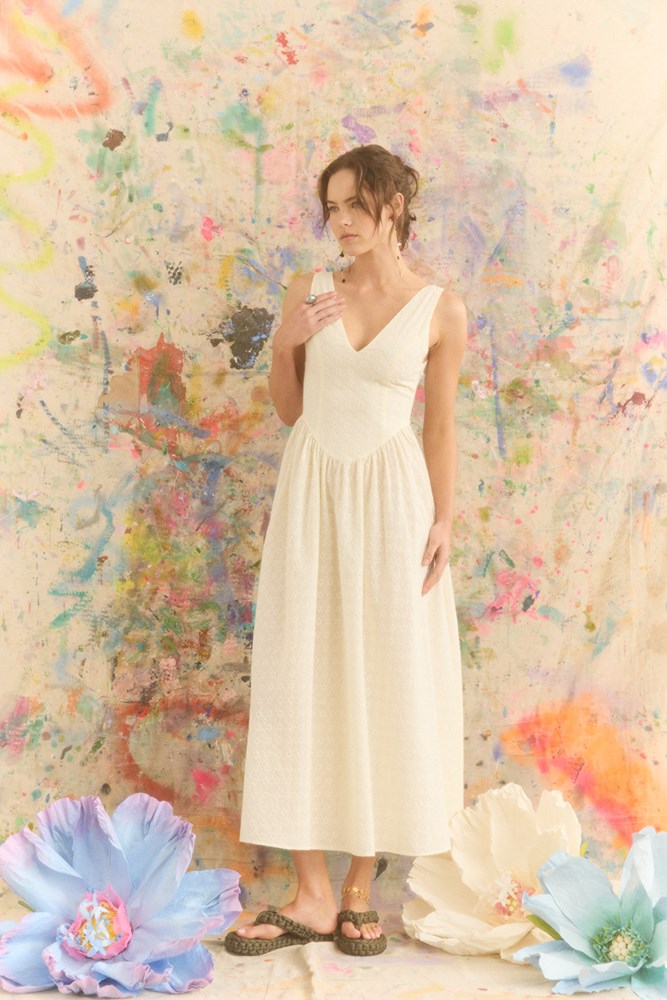 Woman in a white dress standing against a colorful abstract wall.