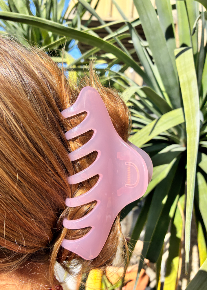Person with pink claw clip in hair against a natural background