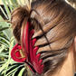 Close-up of a person's hair with a red claw clip against a blurred natural background