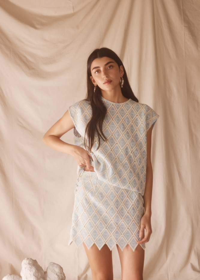 Woman wearing a patterned light blue set against a beige curtain background