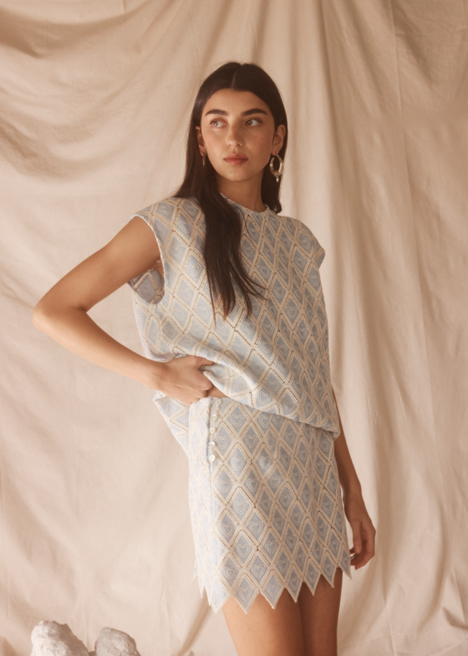 Woman wearing a light blue patterned set against a beige curtain background