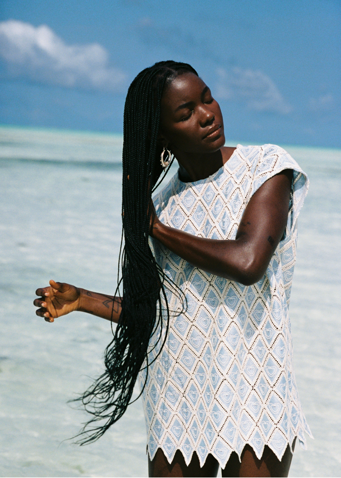 Woman in a baby blue set standing on a beach with clear blue water and sky.