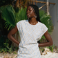 Woman in a light blue patterned dress standing on a sandy beach with palm leaves in the background