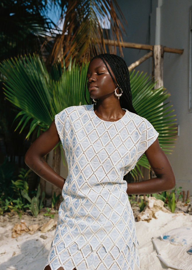 Woman in a light blue patterned dress standing on a sandy beach with palm leaves in the background