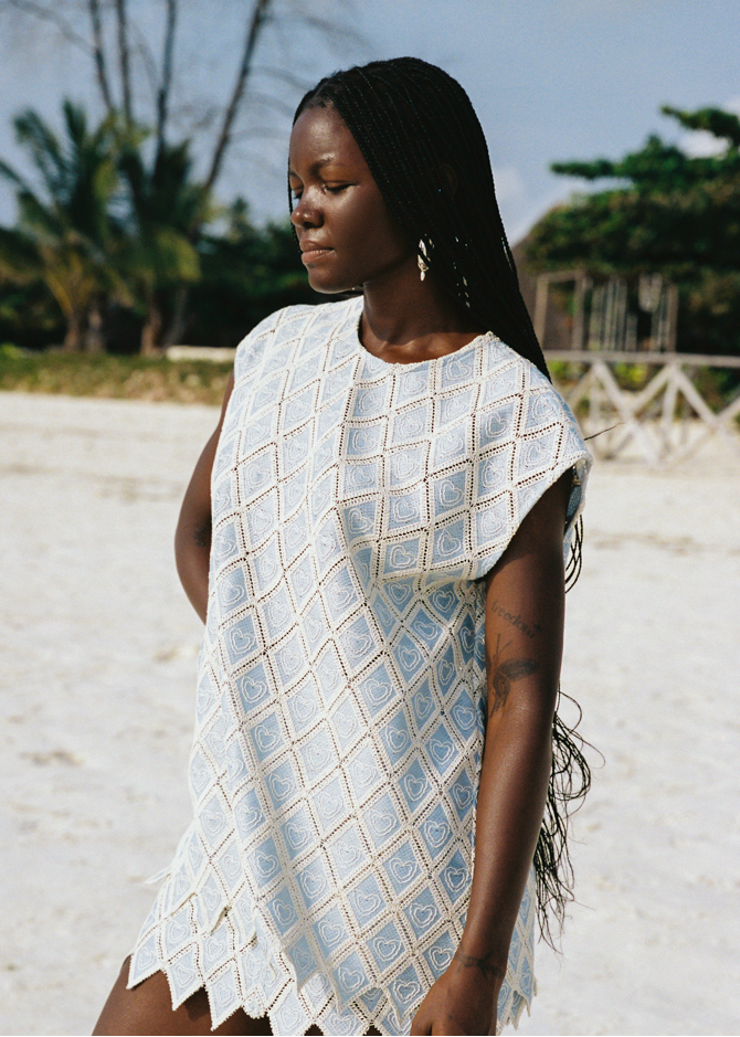 Woman wearing a light blue patterned set standing on a sandy beach with trees in the background