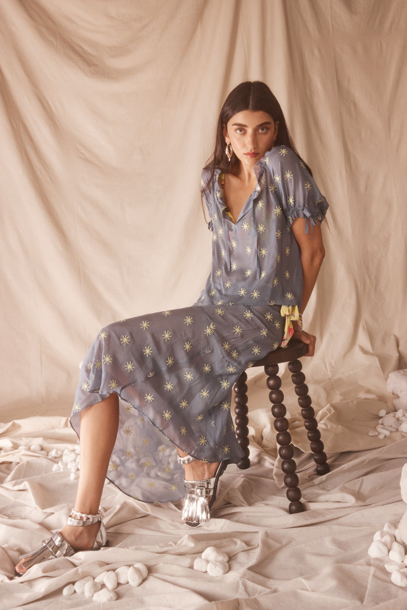 Woman in a sheer, blue blouse and midi skirt set with yellow sun embroided detailing.