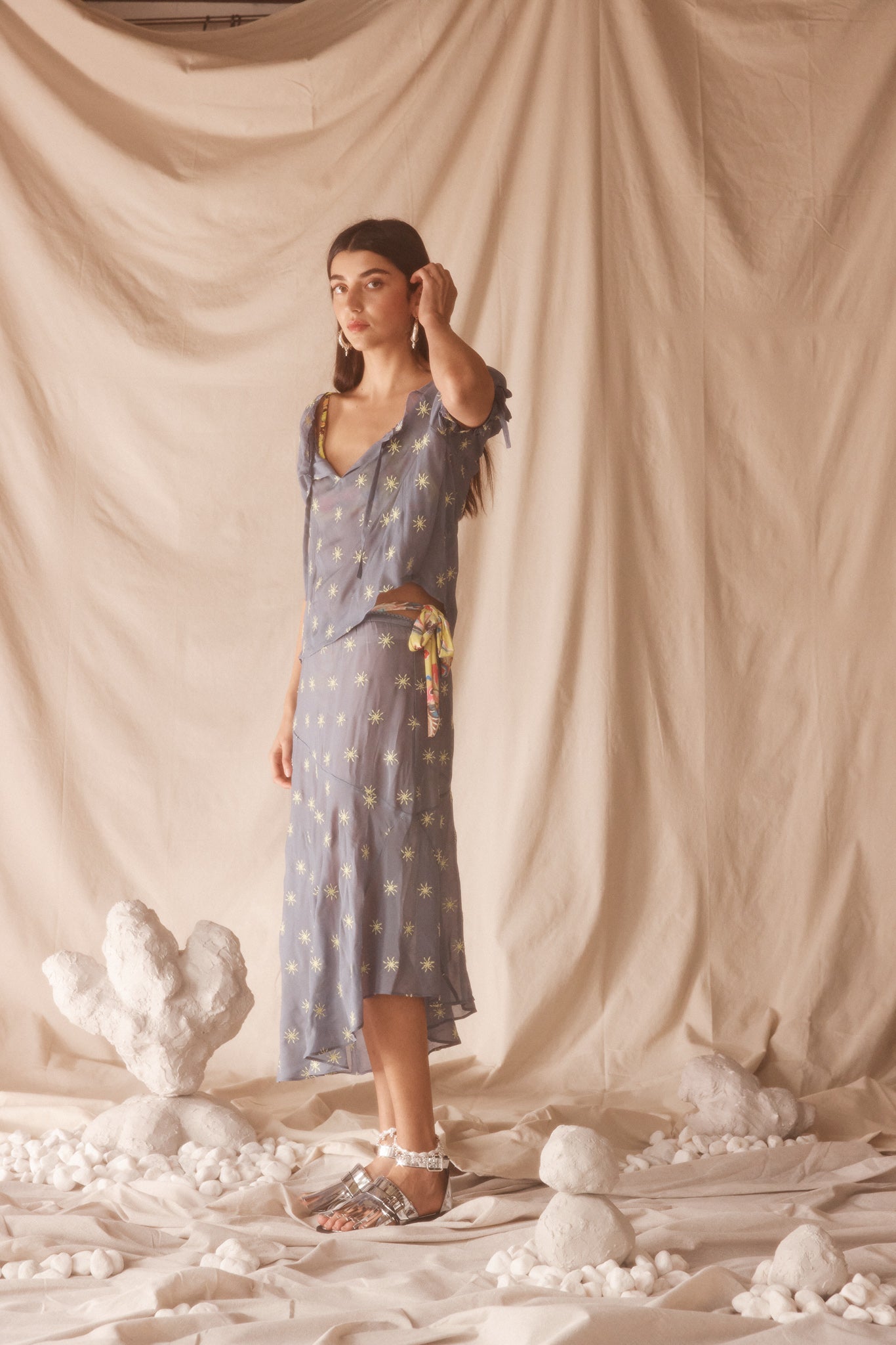 Woman in a sheer, blue blouse and midi skirt set with yellow sun embroided detailing.