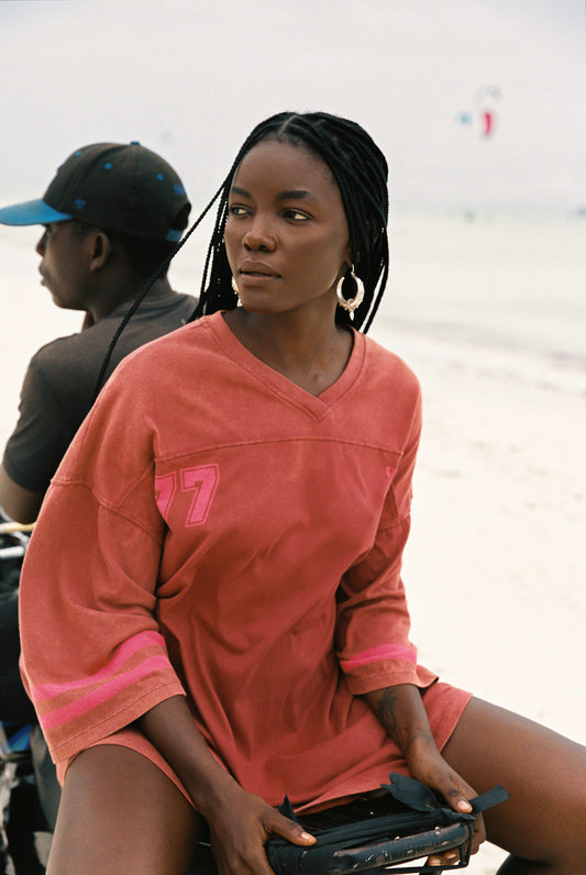 Woman in a red and pink jersey with number 7 sitting on a beach.