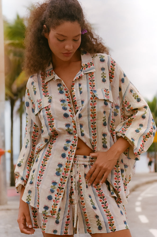 Woman wearing vintage-inspired abstract print in earthy tones; relaxed collared shirt and high-waisted boxer shorts for effortless coastal cool.