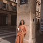 Model leaning against stone pillar under Rue de Rivoli street sign in Paris wearing Kinga Csilla Abracadabra Hades Pant and Abracadabra OG Jumper in burnt orange with sun print