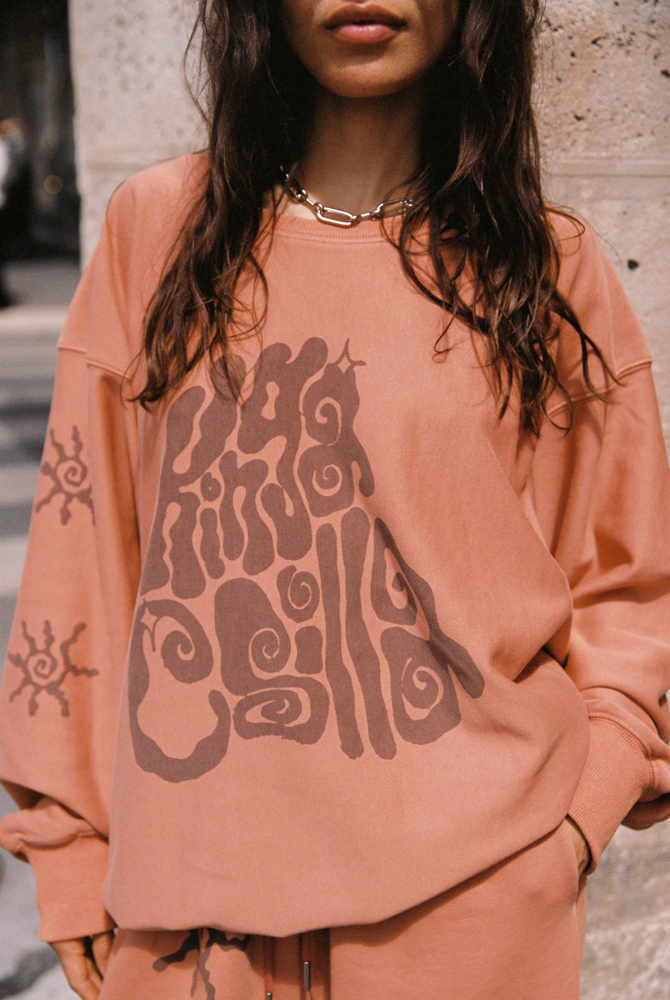 Close-up of Kinga Csilla Abracadabra OG Jumper in terracotta orange with oversized psychedelic logo print and sun motif on sleeve